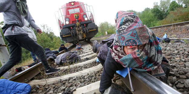 Menschen liegen vor einem stehenden Güterzug auf einer Eisenbahnschiene