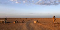 Zwei Männer, die in der Wüste eine Straße mit Autoreifen sperren, am Horizont eine Zeltstadt