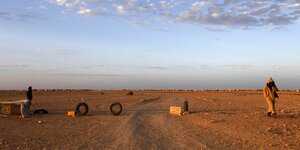 Zwei Männer, die in der Wüste eine Straße mit Autoreifen sperren, am Horizont eine Zeltstadt