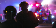 Zwei behelmte und uniformierte Polizisten bei Dunkelheit im vor allem violetten Gegenlicht von Fahrzeugen