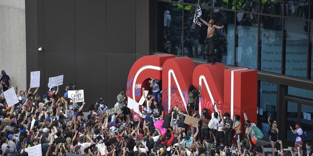 eine riesige Menschenmenge vor der CNN-Zentrale, ein Mann ist auf das überdimensionale CNN-Logo geklettert eine riesige Menschenmenge vor der CNN-Zentrale, ein Mann ist auf das überdimensionale CNN-Logo geklettert