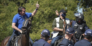 Ein Mann auf einem Pferd grüßt Menschen, einige davon tragen Polizeiuniformen.