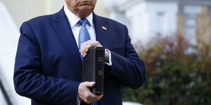 Donald Trump hält ein Buch in der Hand und sieht auf es herab