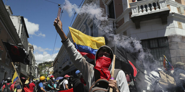 Demonstrierende in Ecuador. Viele tragend Maske, manche Helme aus Schutz. Ein Demonstrant hält einen Bengalo in der Hand. Andere haben Fahnen dabei.