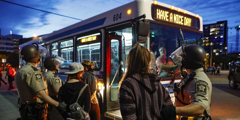 Polizisten stehen mit festgenommenen Demonstranten vor einem Linienbus