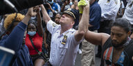 Ein weißer Polizist in New York kniet hin vor Schwarzen Demonstrant:innen.