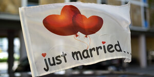 "Just married..." steht auf einer wehenden Fahne, die an einem Autofenster festgemacht ist.