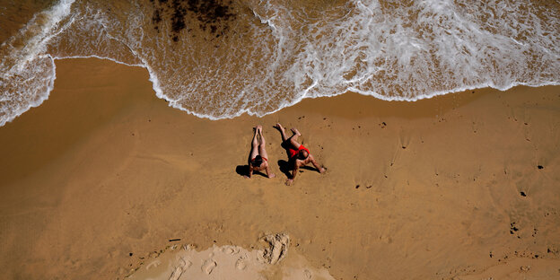 Paar im Sand mit Wellen von oben gesehen