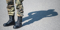 Die Beine eines Menschen in Bundeswehrhofe und Stiefeln. Die person wirft einen Schatten auf Asphalt.