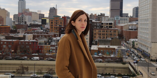Die Autorin Liz Moore im braunen Mantel vor der Skyline von Philadeliphia
