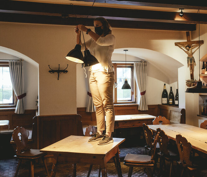 Eine Frau steht auf einem Tisch und bindet zwei Lampen in einem Restaurant zusammen.