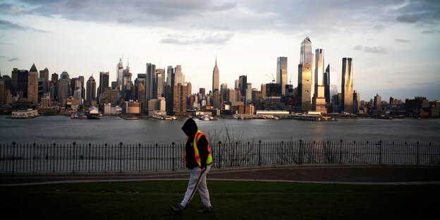 Das Empire State Building und die Skyline von New York mit einem einsamen Mann mit Warnweste davor, der durch einen Park läuft