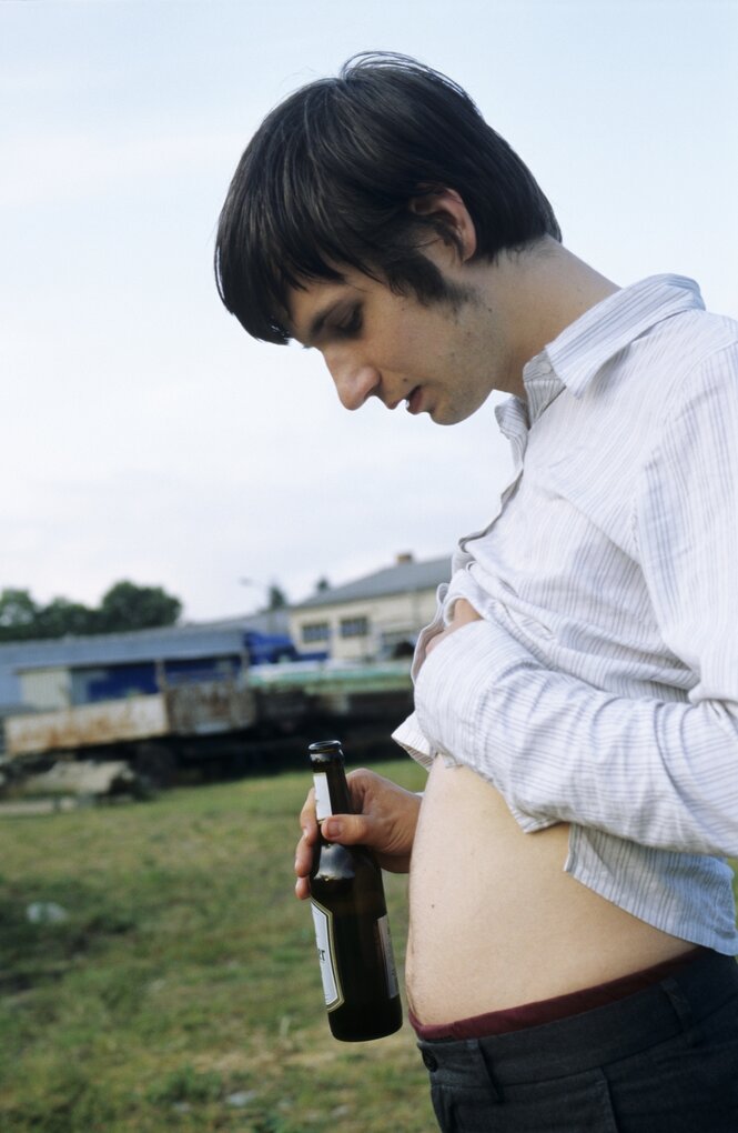 Mann hält sich eine Bierflasche vor den gewölbten Bauch