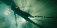 Die Kamera fotografiert von unten eine Person, die im Wasser schwimmt.