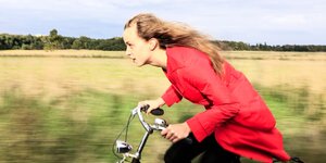 Frau im roten Mantel fährt gegen den Wind Fahrrad