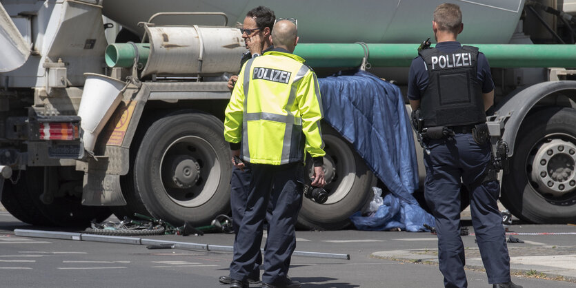 Polizisten stehen vor einem Lkw, unter dessen Reifen Reste eines Rads zu erkennen sind