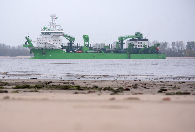 Auf einem Fluss ein grünes Schiff, davor Strand