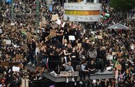 demonstrierende auf dem Berliner Alexanderplatz. sie haben Plakate, teilweise Mundschutz. Eine Menge von Menschen ist auf die Weltzeituhr geklettert und steht oder sitzt dort.