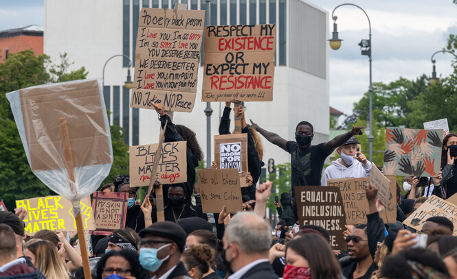 Demonstrierende Menschen in München. Manche sind auf Gegenstände geklettert und ragen aus der Menge heraus.