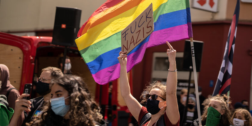Eine Gruppe von Gegendemonstrantinnen. Eine hält ein Schild in die Luft, auf dem "Fuck Nazis" steht. Sie hält ihre Mittelfinger in die Luft. Hinter hier eine Regenbogenfahne.