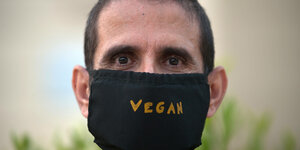 Mann mit schwarzem Mund-Nasen-Schutz auf dem "Vegan" steht