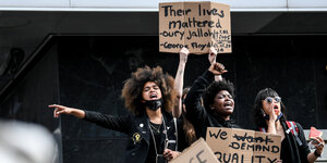 Drei Demonstrantinnen halten Schilder