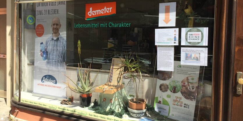 Ein Schaufenster mit Demeterlogo, daneben hängen beschriebene Din A-4-Seiten