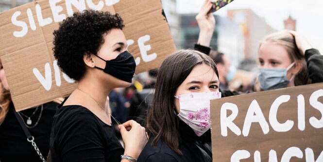 Demonstrantinnen mit Schildern auf denen unter anderem Racism Sucks steht