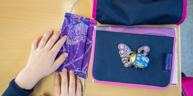 Schulkinder-Hände die eine Atemschutzmaske neben ein Fedemäppchen legen
