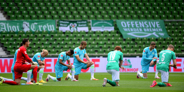 Spieler von Werder Bremen und dem VfL Wolfsburg Knien auf dem Spielfeld, die Ränge im Hintergrund sind leer