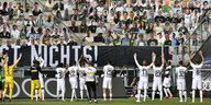eine Fußballmannschaft feiert vor einer Tribüne, auf der Fans aus Pappe stehen