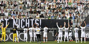 eine Fußballmannschaft feiert vor einer Tribüne, auf der Fans aus Pappe stehen