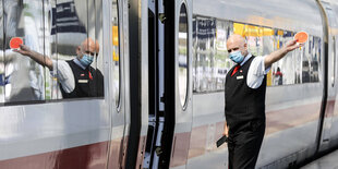 Ein Schaffner mit Mundschutz gibt den Zug zur Abfahrt frei.