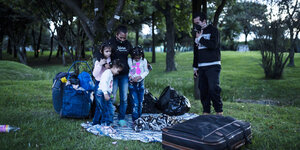 Eine Familie sitzt mit ihrem Gepäck auf dem Boden