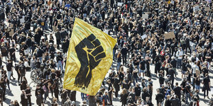 Eine Goildene Fahne mit einer schwarzen Faust inmitten tausender Demonstranten.