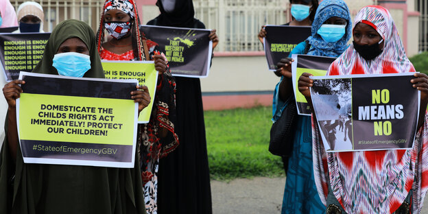 Frauen mit Mundschutz und Plakaten bei einer Demonstration.
