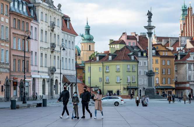 Passanten mit Mund-Nase-Schutz gehen über einen Platz in der Altstadt von Warschau