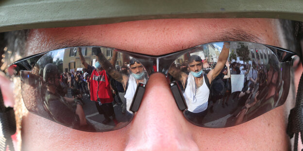 Demonstranten spiegeln sich in den Brillengläsern eines Uniformierten