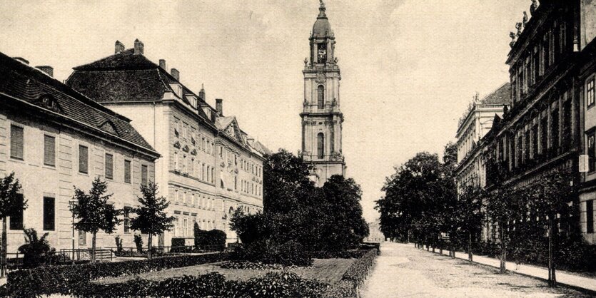 Eine Straße mit klassizistischen Fassade läuft auf einen Kirchturm zu.