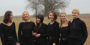 Sechs Frauen auf freiem Feld, schwarze Anziehsachen, ein Baum im Hintergrund