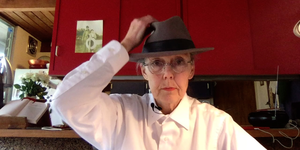 Anne Carson mit Hut vor einem roten Regal.