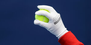 Eine behandschuhte Hand hält einen Tennisball