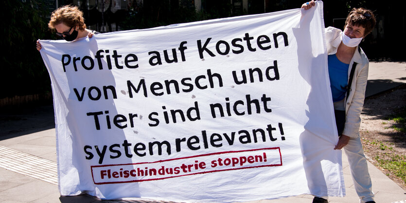 Zwei Menschen halten ein Transparent mit der Aufschrift: Profite auf Kosten von Mensch und Tier sind nicht systemrelevant - Fleischindustrie stoppen"