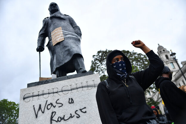 Eine Person mit erhobener Faust steht vor einer Statue.