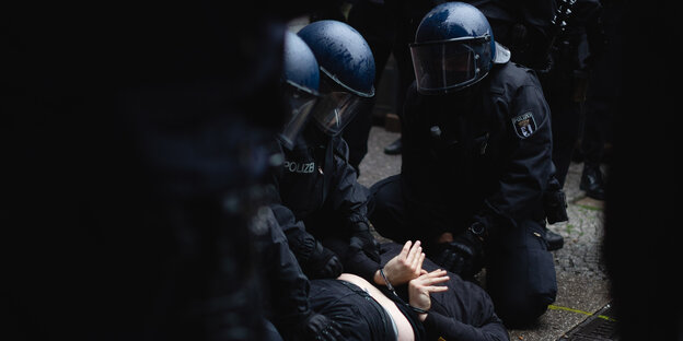 Mehrere Polizisten in Schutzmontur knienen auf einer am Boden liegenden Person