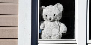 Ein weißer Teddybär sitzt stumm in einem Fenster
