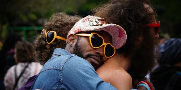 ein Mann mit Sonnenbrille in Herzform umarmt einen anderen Mann von hinten