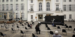 Stühle mit Abstand stehen vor einer kleinen Bühne draußen vor einem Theater.