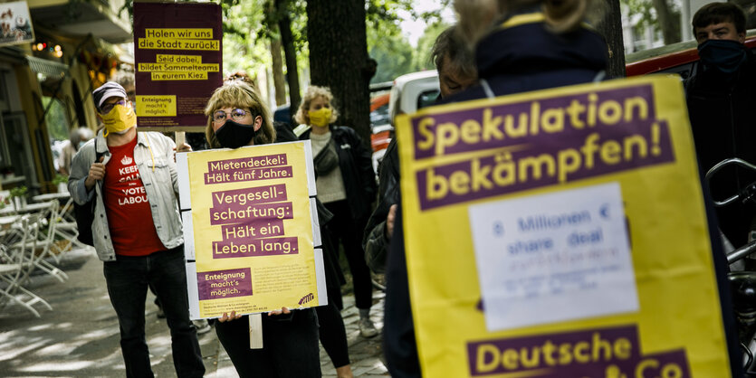 Miet-Aktivist:innen auf einer Demo für Vergesellschaftung von Wohnraum: Eine Frau mit Mundschutz trägt ein Schild.