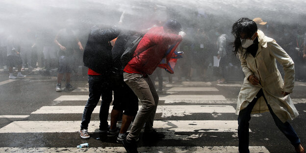 Junge Protestierende stehen im Strahl von Wasserwerfern